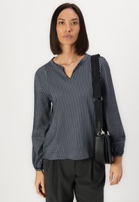 Navy and white striped long-sleeve blouse features a v-neckline and fitted cuffs, paired with dark gray trousers and a black crossbody bag.
