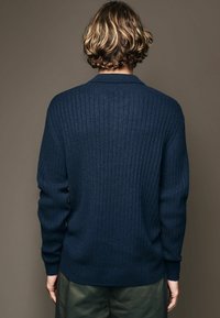 Marineblaues geripptes Sweatshirt mit Rundhalsausschnitt, langen Ärmeln und geradem Saum. Weiche Textur mit dezentem Glanz. Einfaches Design.