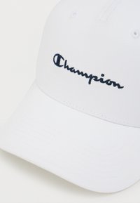 Λευκό βαμβακερό καπέλο μπέιζμπολ με καμπυλωτό γείσο και κεντημένο μπλε σκούρο λογότυπο "Champion" στο μπροστινό μέρος. Διαθέτει ραμμένες τρύπες αερισμού.