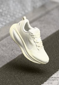 Scarpa da corsa Nike bianca, tomaia testurizzata, design con lacci, suola ammortizzata, punta arrotondata, con logo distintivo e accenti sottili.