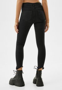 Jeans skinny negros con dobladillos deshilachados, que cuentan con una cintura alta, diseño de cinco bolsillos y una textura de denim suave. Llevados con botas negras gruesas de cordones.