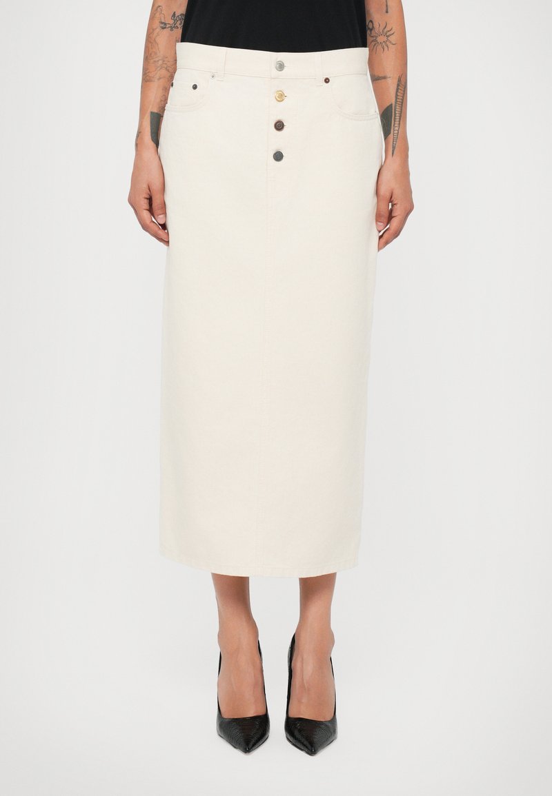 Falda midi de mezclilla blanca con corte recto, con cierre de botones, cinco bolsillos y detalles de costura sutiles. Combinada con tacones negros de punta.