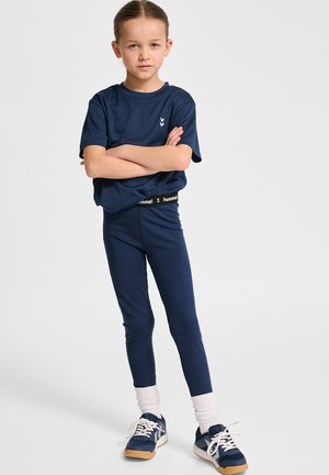 Granatowy t-shirt sportowy z krótkimi rękawami, zestawiony z granatowymi legginsami i niebieskimi sneakersami. Legginsy mają czarny, markowy pas.