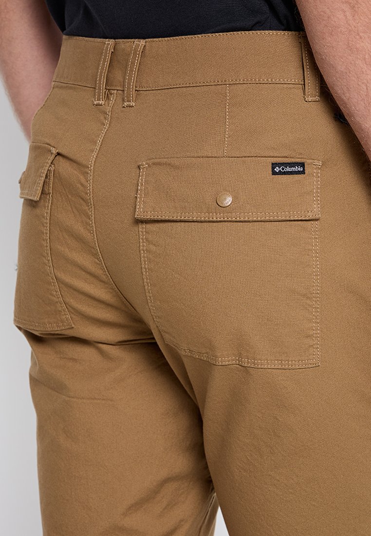 Pantalones cargo color beige, hechos de tela duradera, con dos bolsillos con solapa en la parte posterior y una pequeña etiqueta de logo de Columbia encima de uno de los bolsillos.