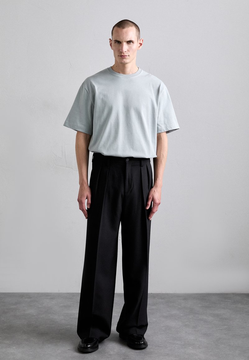 Light blue short-sleeve t-shirt with a relaxed fit, paired with black pleated trousers. Smooth textures, minimalist design, and tailored silhouette.