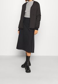 Czarna pikowana kurtka typu bomber, szary sweter, czarna spódnica midi i czarne botki za kostkę. Gładka faktura, prosty design i monochromatyczna kolorystyka.