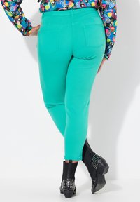 Tyrkysové úzké džíny z elastického materiálu, slim fit, se dvěma zadními kapsami, doplněné černými kotníkovými botami se stříbrnými cvočky.