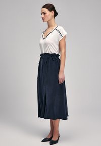 Camiseta blanca de cuello en V con ribete azul, combinada con una falda midi fluida de un azul marino oscuro, con cintura ligera y aberturas laterales. Diseño elegante y sencillo.