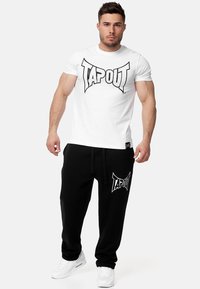 White cotton t-shirt with a large black "TAPOUT" logo, paired with black joggers featuring the same logo, finished with white sneakers.