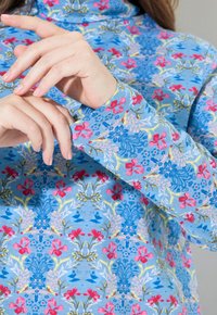 Blaues Langarmoberteil mit floralem Muster und Schalkragen. Verfügt über abwechslungsreiche florale Designs in Pink, Blau und Grün sowie eine weiche Stofftextur.