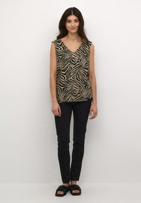 Top sans manches en imprimé zèbre beige et noir, avec un design en V. Associé à un pantalon slim noir et des sandales noires à enfiler.