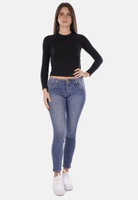 Top nero a maniche lunghe dal design aderente abbinato a jeans skinny azzurri chiari e sneakers bianche, con un classico stile a cinque tasche.