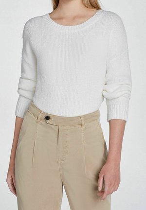 Suéter blanco de punto con escote redondo y mangas largas enrolladas, combinado con unos chinos beige que tienen un botón frontal y pinzas.