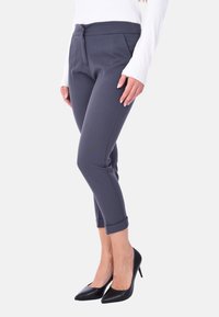 Pantaloni grigi su misura con una finitura in tessuto liscia, pieghe sottili e orli arrotolati, abbinati a tacchi neri a punta.