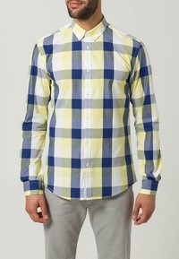 Camicia a maniche lunghe con bottoni, in un motivo a quadri giallo, bianco, blu e verde. Realizzata in stoffa con una trama liscia.