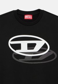 Crna majica s velikim bijelim Diesel logotipom i suptilnim gradijentnim sjenčanim efektom. Rebrasti ovratnik i mekana tekstura tkanine.