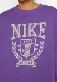 Purple cotton sweatshirt featuring distressed white Nike logo, "Oregon," and decorative laurel design at the chest. Round neckline.