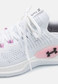 Hvide sportsko med tekstureret stof, pink detaljer, sort logo og hvide snørebånd. Har en spraglet sål og mesh-detaljer.