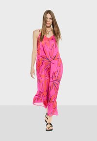 Pink floral maxi dress with spaghetti straps, featuring a loose fit and flowing fabric. Black strappy sandals complete the outfit.