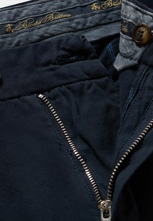 Navyblaue Hose mit Reißverschluss, mit glatter Textur, kontrastierendem Innenfutter und braunem Knopfdetail mit goldener Markenkennung.