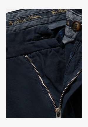 Navyblaue Hose mit Reißverschluss, mit glatter Textur, kontrastierendem Innenfutter und braunem Knopfdetail mit goldener Markenkennung.