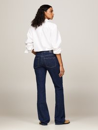 Uppflakade jeans i mörk tvätt med en slät textur. Matchat med en vit långärmad skjorta med krage och neutrala skor.