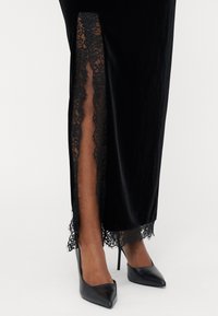 Fekete bársonydressz csipkés oldalszélekkel, sima tapintással. Fekete hegyes orrú magassarkúval viselve. Elegáns és testhezálló fazon.