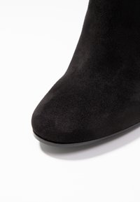 Sort ruskind ankelstøvle med spids tå, glat tekstur og en let hæl, med et sømløst design og uden synlige pynt.