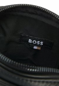 Interno di tessuto nero di una borsa, con etichetta bianca con logo "BOSS" e una cerniera a contrasto. Texture liscia con design minimalista.