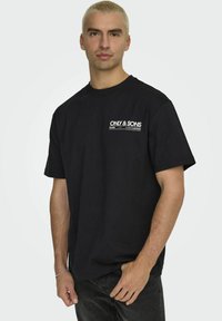 T-shirt in cotone nero con stampa bianca che riporta la scritta "ONLY & SONS" sul lato sinistro del petto. Maniche diritte e vestibilità comoda.