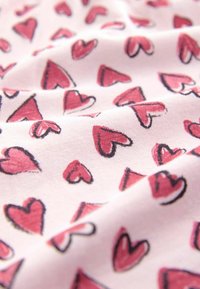 Bomuldsstof i blød pink med et gentaget mønster af røde hjerter omkranset af sort, med en glat tekstur og let stræk.