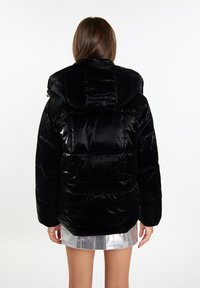 Giacca a vento nera con una texture lucida e trapuntata e cappuccio over-size. Presenta una vestibilità rilassata e grandi tasche posteriori.