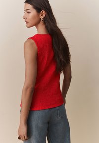Rode mouwloze top van textuurstof, getailleerd ontwerp en ronde halslijn, gecombineerd met high-waisted denimbroeken.