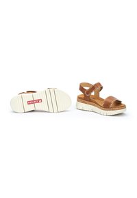 Sandalias de cuero marrón con una correa ancha, costuras blancas y una suela acolchada. Cuenta con una correa ajustable para un ajuste seguro.