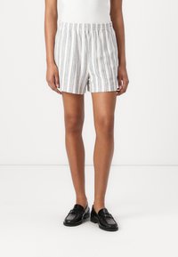 Stripete shorts i lett stoff med elastisk midje, med vertikale blå og hvite striper, kuttet over kneet. Svarte loafers brukt.