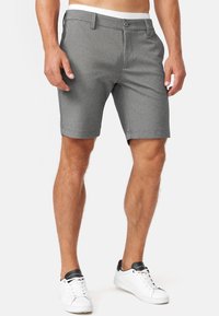 Grijze shorts van gestructureerde stof, met een knoopsluiting, ceintuurlussen en een getailleerde pasvorm. G gedragen met witte sneakers.