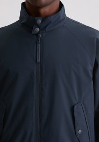 Granatowa kurtka wykonana z gładkiego, wodoodpornego materiału. Posiada stójkę, przedni zamek błyskawiczny oraz zatrzaski na kieszeniach.