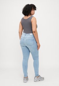 Body gris ajustado combinado con pantalones vaqueros skinny azul claro y zapatillas grises. Textura brillante en las zapatillas, diseño minimalista en la ropa.