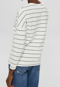 Camicia a maniche lunghe in cotone con base bianca e righe orizzontali grigie scure, caratterizzata da un collo rotondo e una vestibilità comoda. Abbinata a jeans di denim.