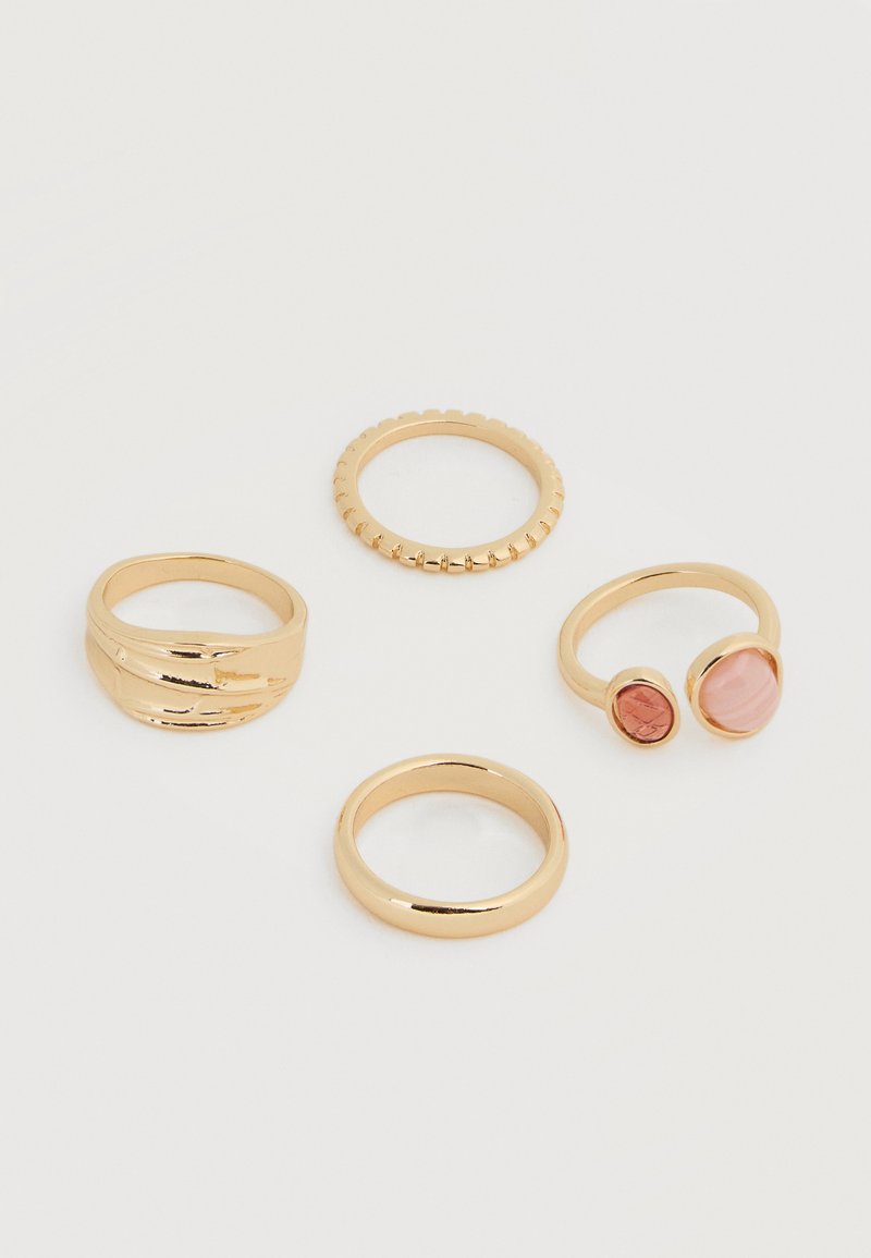 Τέσσερα χρυσά δαχτυλίδια σε λευκή επιφάνεια: ένα με δύο ροζ πέτρες, ένα απλό, ένα με υφή στις άκρες και ένα με διπλωτό σχέδιο.