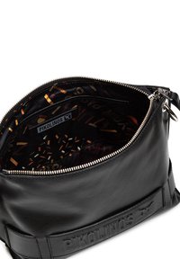 Czarna skórzana torba z zamkiem błyskawicznym, z dekoracyjną podszewką wnętrza w różne wzory oraz widoczną metką marki.