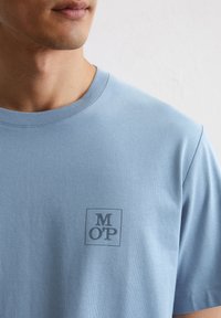 Lichtblauw katoenen t-shirt met een ronde halslijn en korte mouwen. Bevat een klein donkerblauw logo binnen een vierkant op de borst.