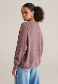 Pulover tricotat supradimensionat în nuanță subtilă de mauve, cu un design texturat și umeri căzuți. Asortat cu blugi din denim albastru deschis.