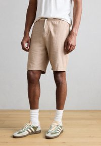 Μπεζ λινά σορτς με ελαστική μέση και κορδόνι. Συνδυασμένα με πράσινα, κρεμ και ροζ ρετρό αθλητικά παπούτσια και λευκές κάλτσες μέχρι τον αστράγαλο.