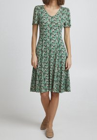 Robe florale verte à manches courtes, décolleté en V et jupe évasée. Fabriquée en tissu doux avec de petits motifs de feuilles denses.