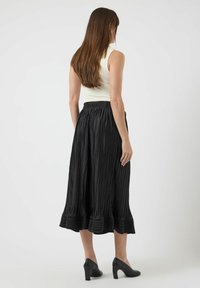 Sort plisseret midinederdel med tekstureret finish, med en udvidet kant og elastisk taljebånd, kombineret med sorte hælede sko.