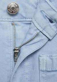 Svietlo modrá džínovina s viditeľným zipsom a strieborným gombíkom. Textúra je hladká s klasickým dizajnom džínsov a malou detailnou kapsičkou.