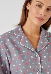 Grijs fleece pyjamashirt met meerkleurige stippen in rood, roze en blauw. Bevat een notch-kraag en witte bies langs de randen.