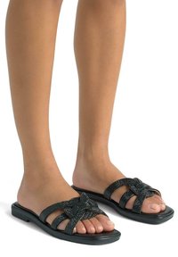 Ciabatte nere con upper texturizzato e un design a nodo. Suola piatta con più cinturini, che mettono in risalto una finitura liscia e lucida.