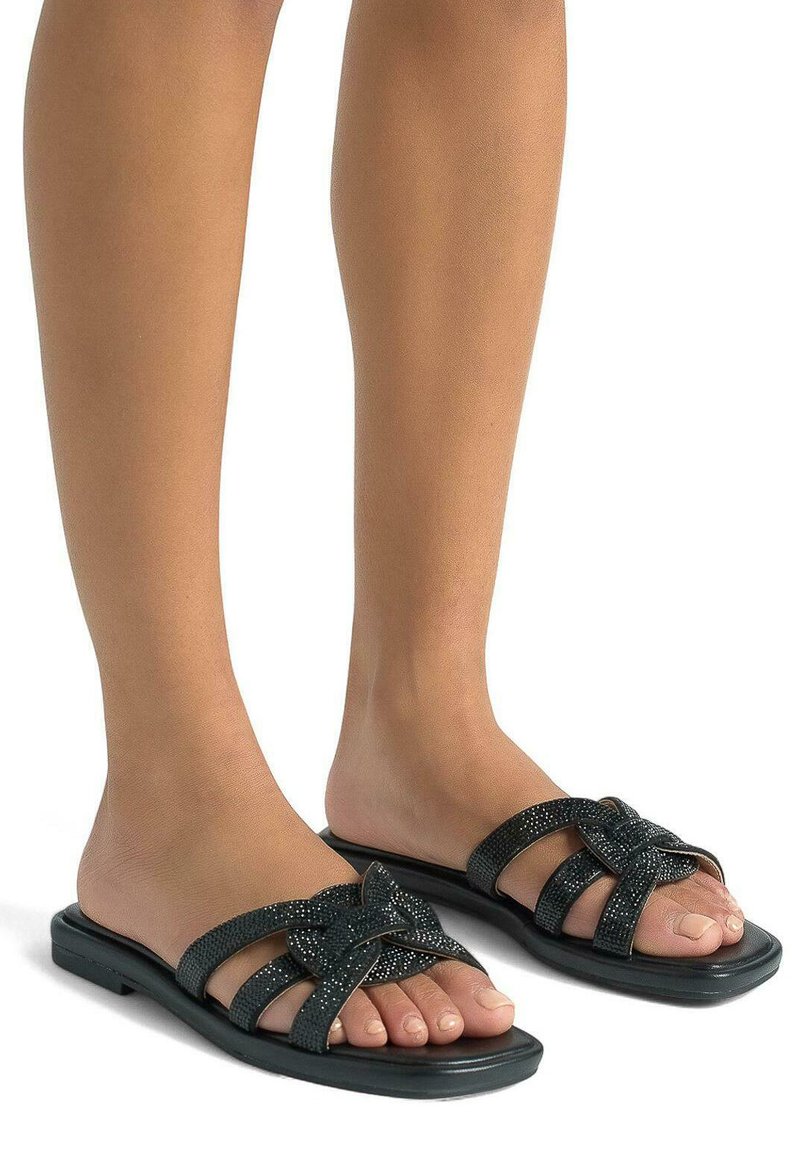 Ciabatte nere con upper texturizzato e un design a nodo. Suola piatta con più cinturini, che mettono in risalto una finitura liscia e lucida.